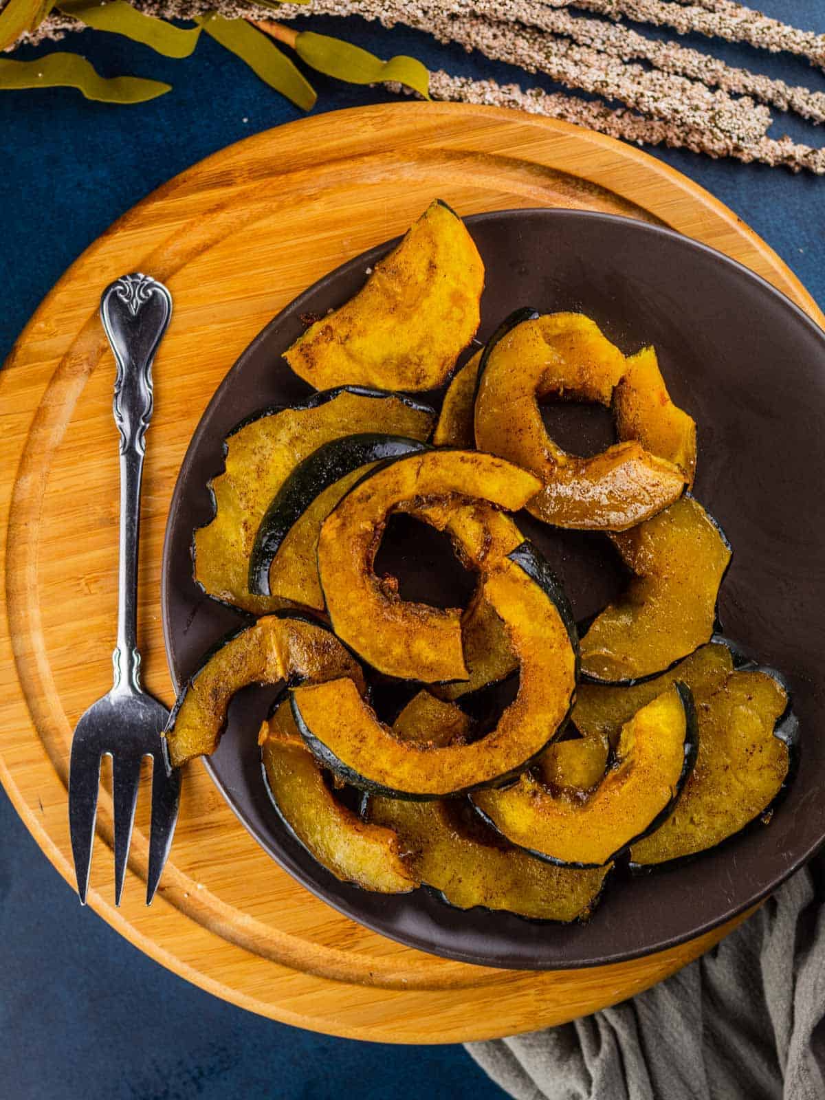 roasted acorn squash slices on a brown plate on a wooden tray with a serving fork