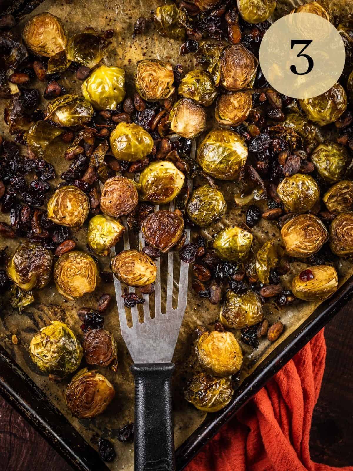 metal spatula holding a scoop of balsamic roasted brussels sprouts on a sheet pan