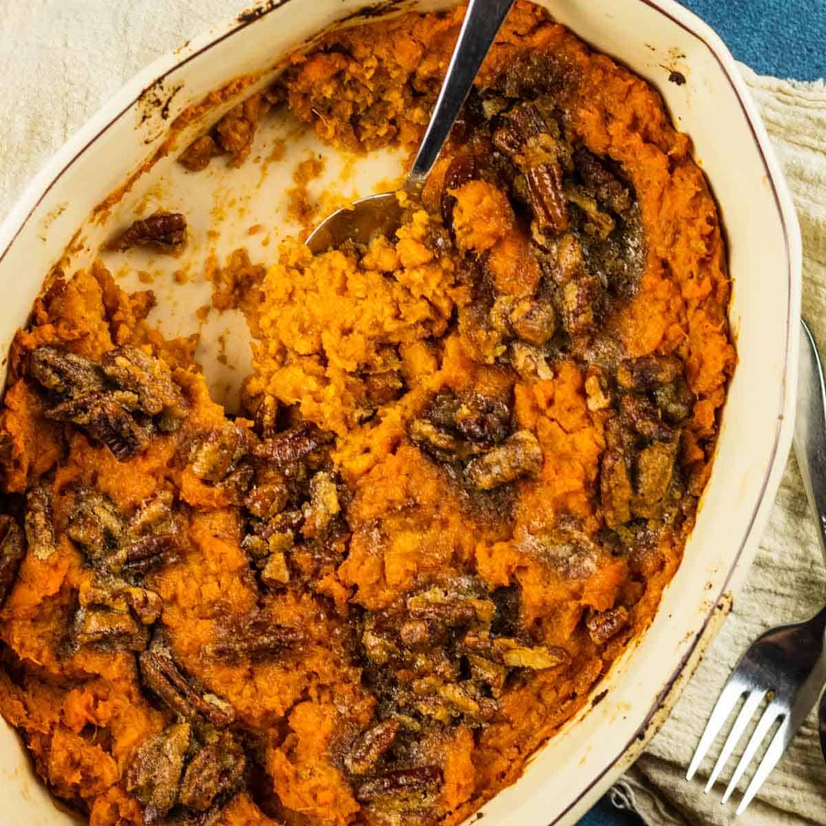 oval dish filled with sweet potato casserole topped with pecans with a spoon scooping them out