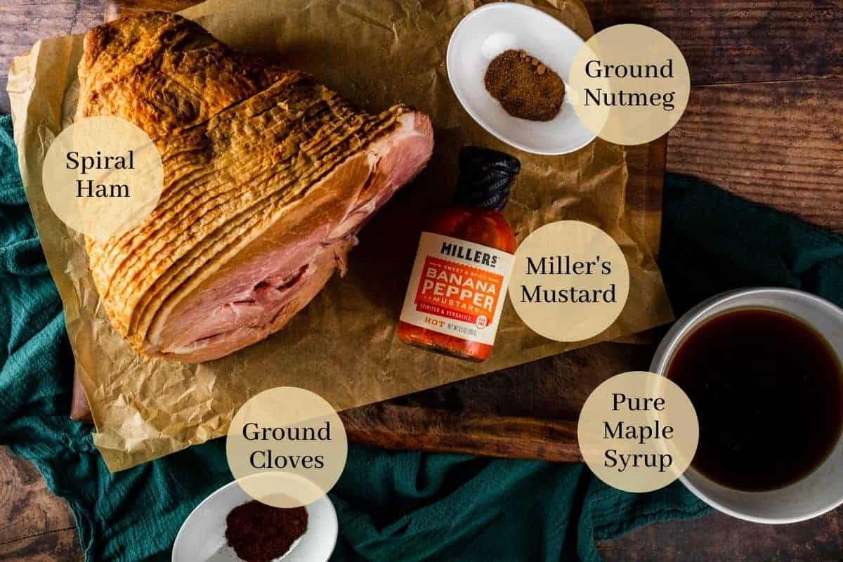 spiral ham, bottle of millers mustard, ground nutmeg, ground cloves and maple syrup in white dishes
