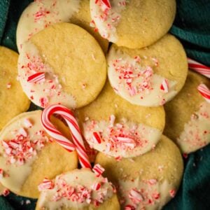 pile of circle shortbread cookies dipped half in white chocolate and topped with crushed peppermint candy
