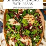 large spinach salad on a brown wooden tray with pears, pomegranate seeds, cheese and pecans