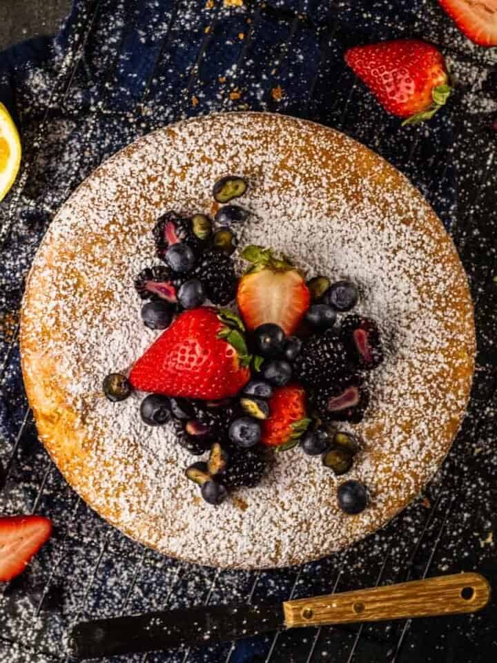 round olive oil cake topped with powdered sugar and fresh berries