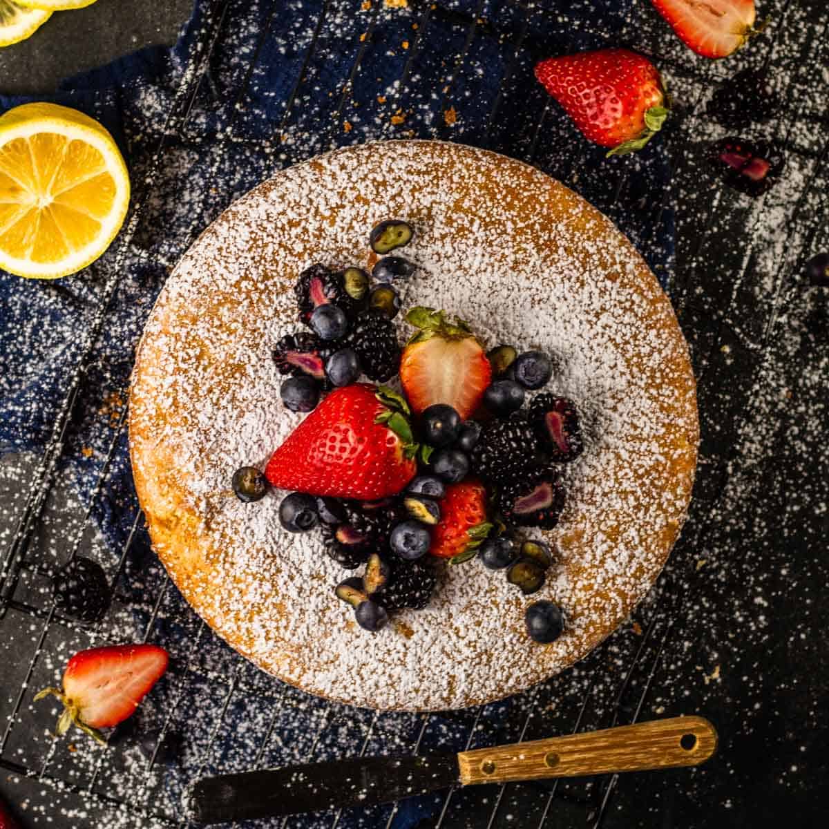 round cake on a cooling rack covered with powdered sugar and fresh berries