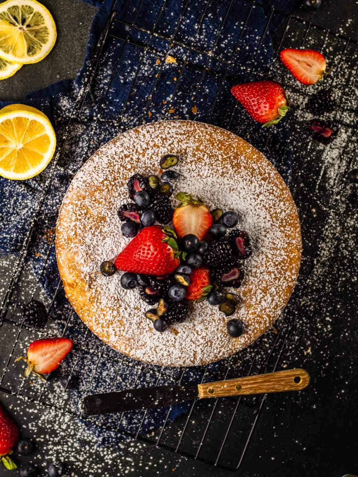 round olive oil cake topped with powdered sugar and fresh berries on a cooling rack