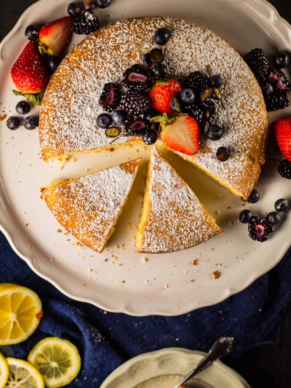 round cake covered in powdered sugar and berries with two slices cut from it