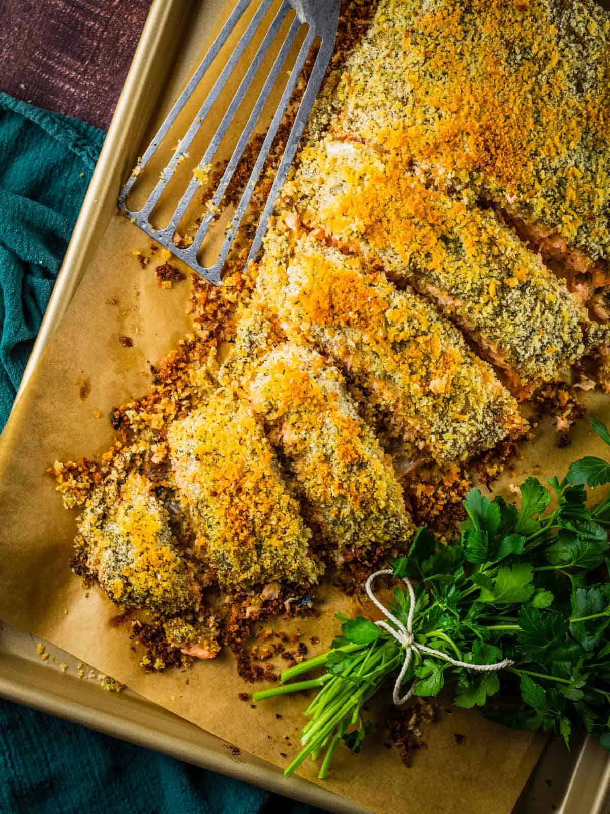 fiilet of panko crusted salmon partially sliced on a sheet pan with a metal spatula