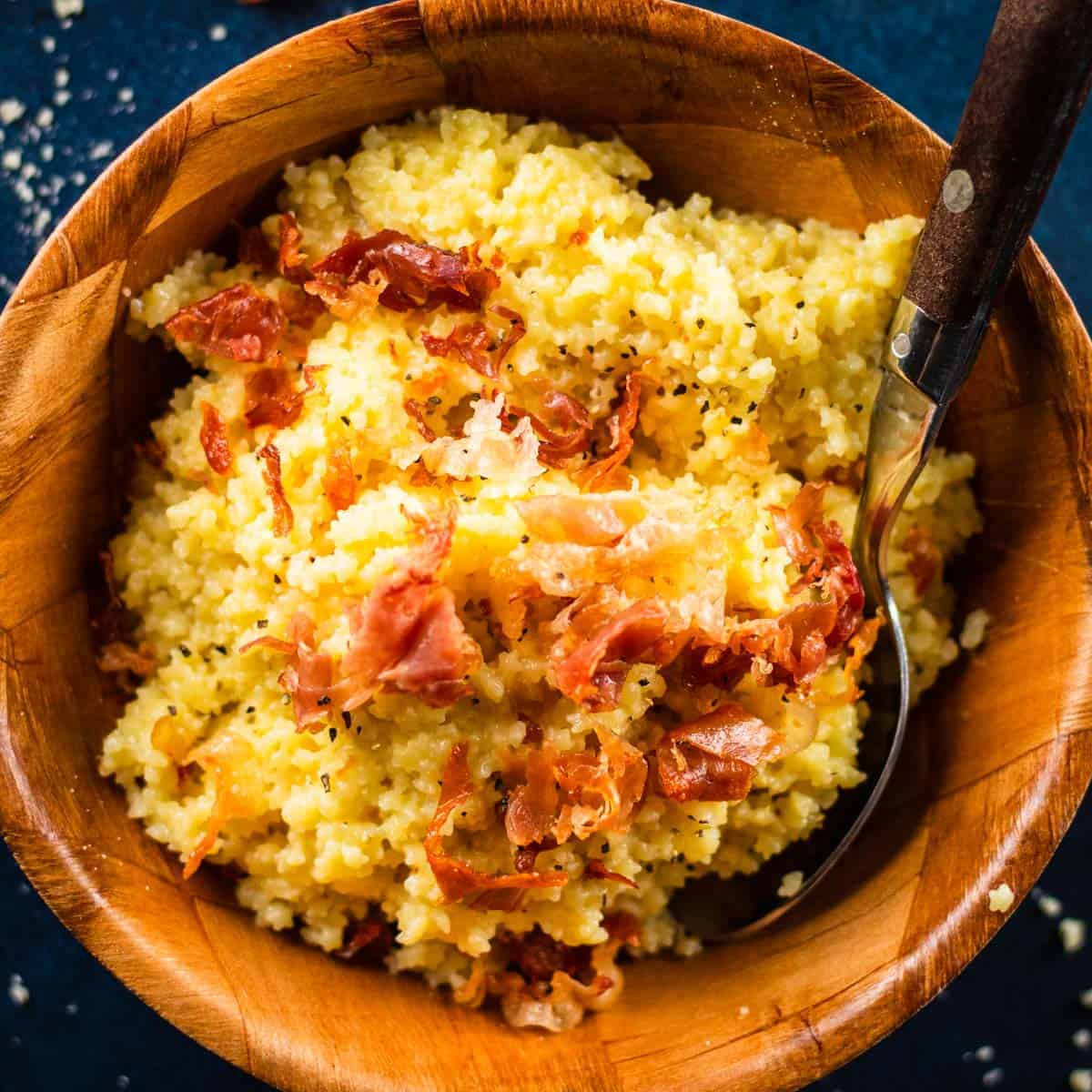wooden bowl filled with cheesy pastina pasta topped with crispy prosciutto