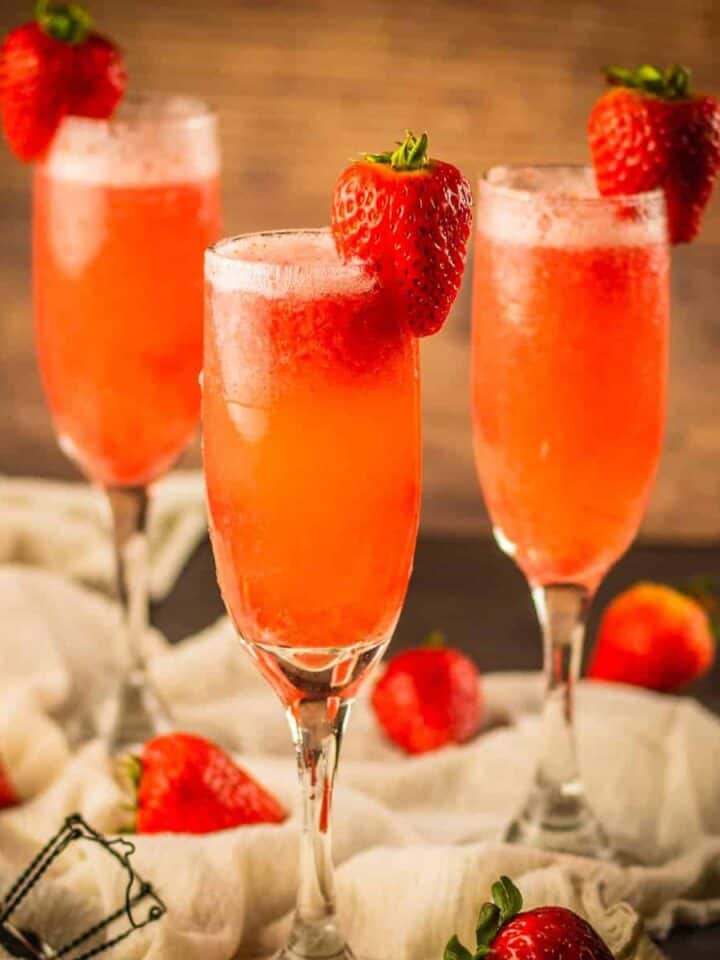 three champagne flutes filled with prosecco and strawberry puree and garnished with a fresh strawberry