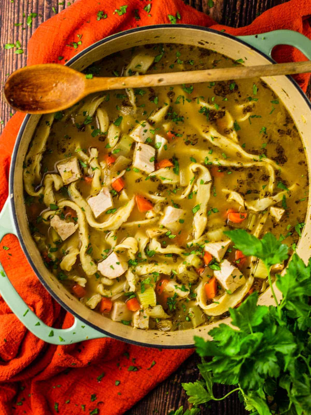 dutch oven pot of chicken nooodle soup with a wooden spoon resting on top