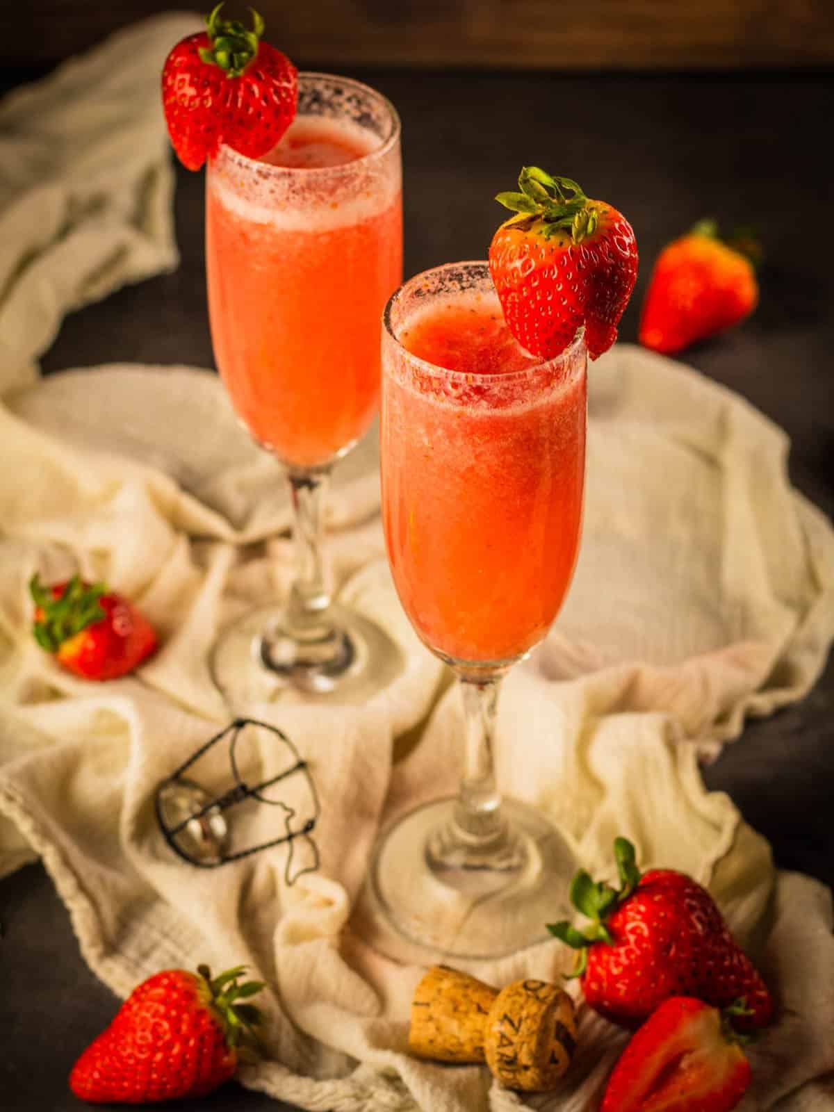 two champagne flutes filled with rossini cocktail and garnished with fresh strawberries and strawberries around 