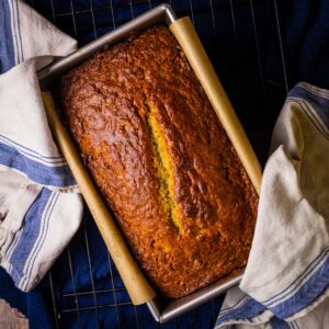 banana bread in a loaf pan with white and blue towels holding it