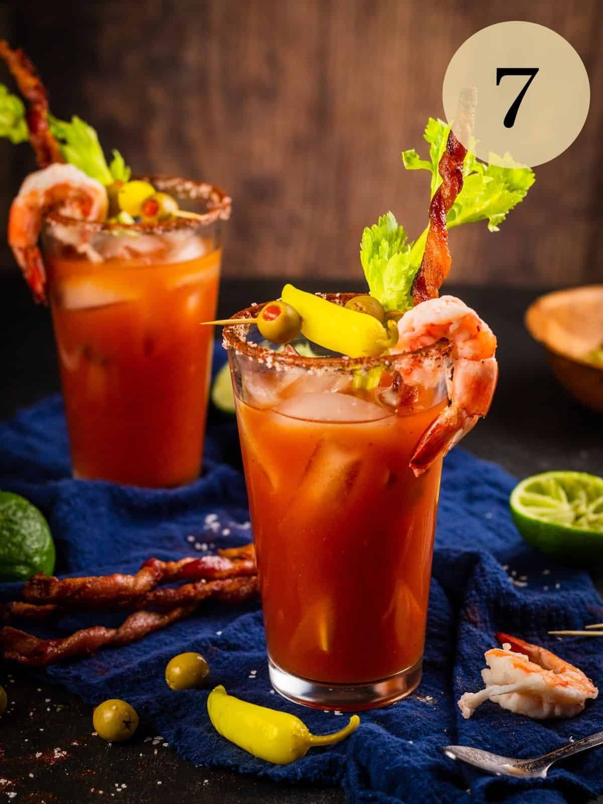 bloody marys in clear glasses garnished with bacon, celery, shrimp, olives and peppers