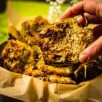 hand holding a roasted artichoke with parmesan cheese baked in it