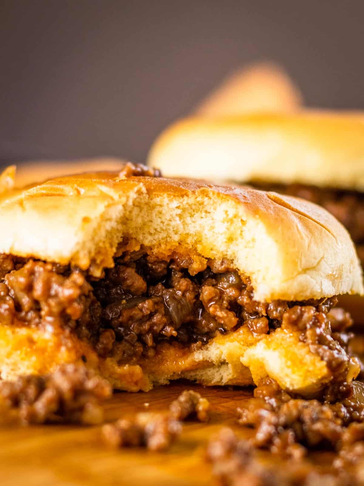 sloppy joe sandwich on wooden tray with a bite taken from it and meat spilling out.