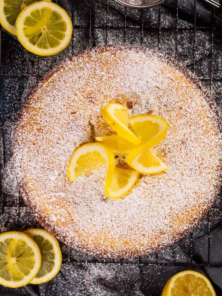 lemon ricotta cake dusted in powdered sugar and garnished with fresh lemon wheels.
