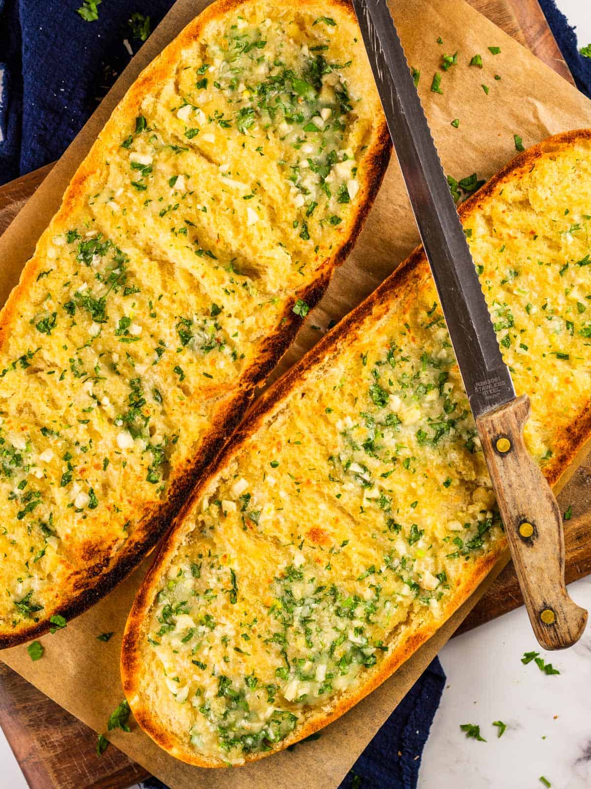 halved italian bread toasted with garlic, herbs and cheese and a knife resting on top.