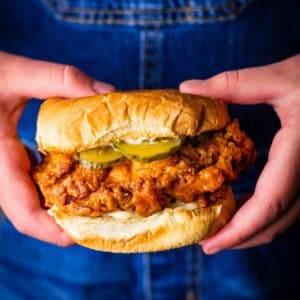 hands holding a buttermilk fried chicken sandwich topped with pickles and mayo.