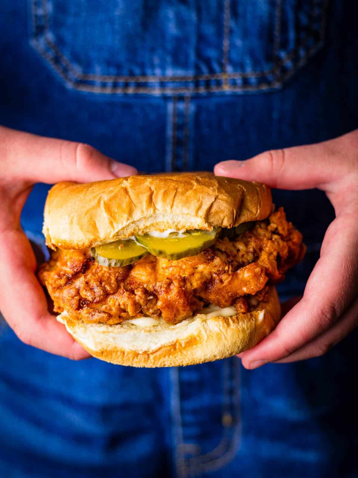 two hands holding a fried chicken sandwich topped with pickles and mayo on a toasted bun.