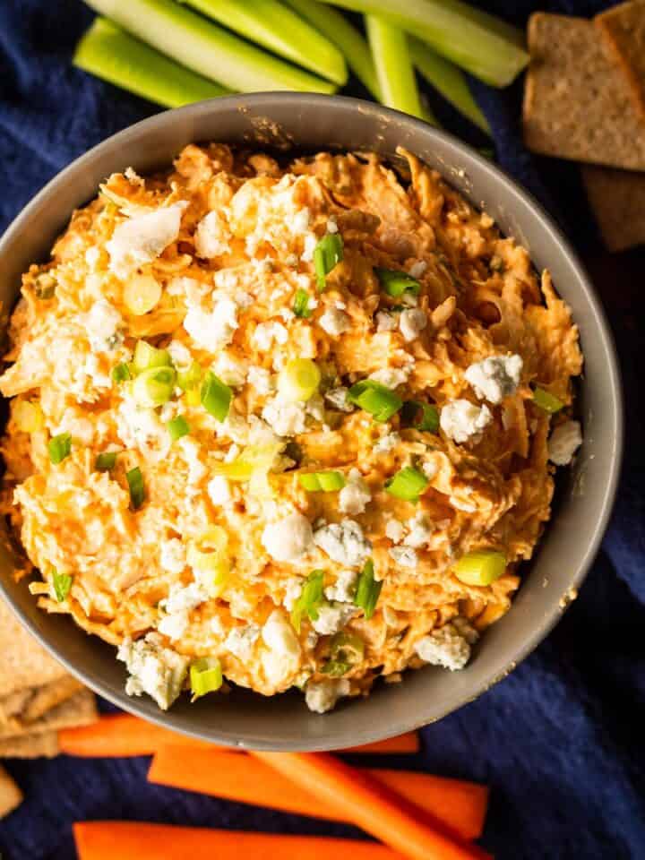 buffalo chicken dip in a bowl topped with blue cheese and green onions.