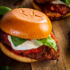 chicken parm sandwich on a cutting board with mozzarella, sauce and fresh basil.