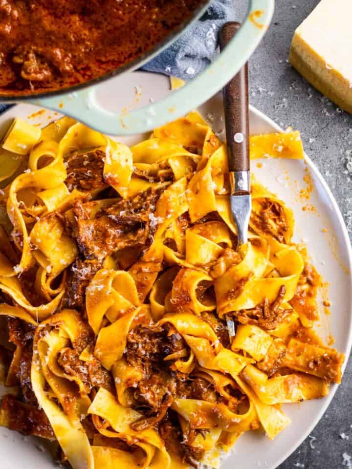 pappardelle pasta with short rib ragu on a gray plate with a fork in it.