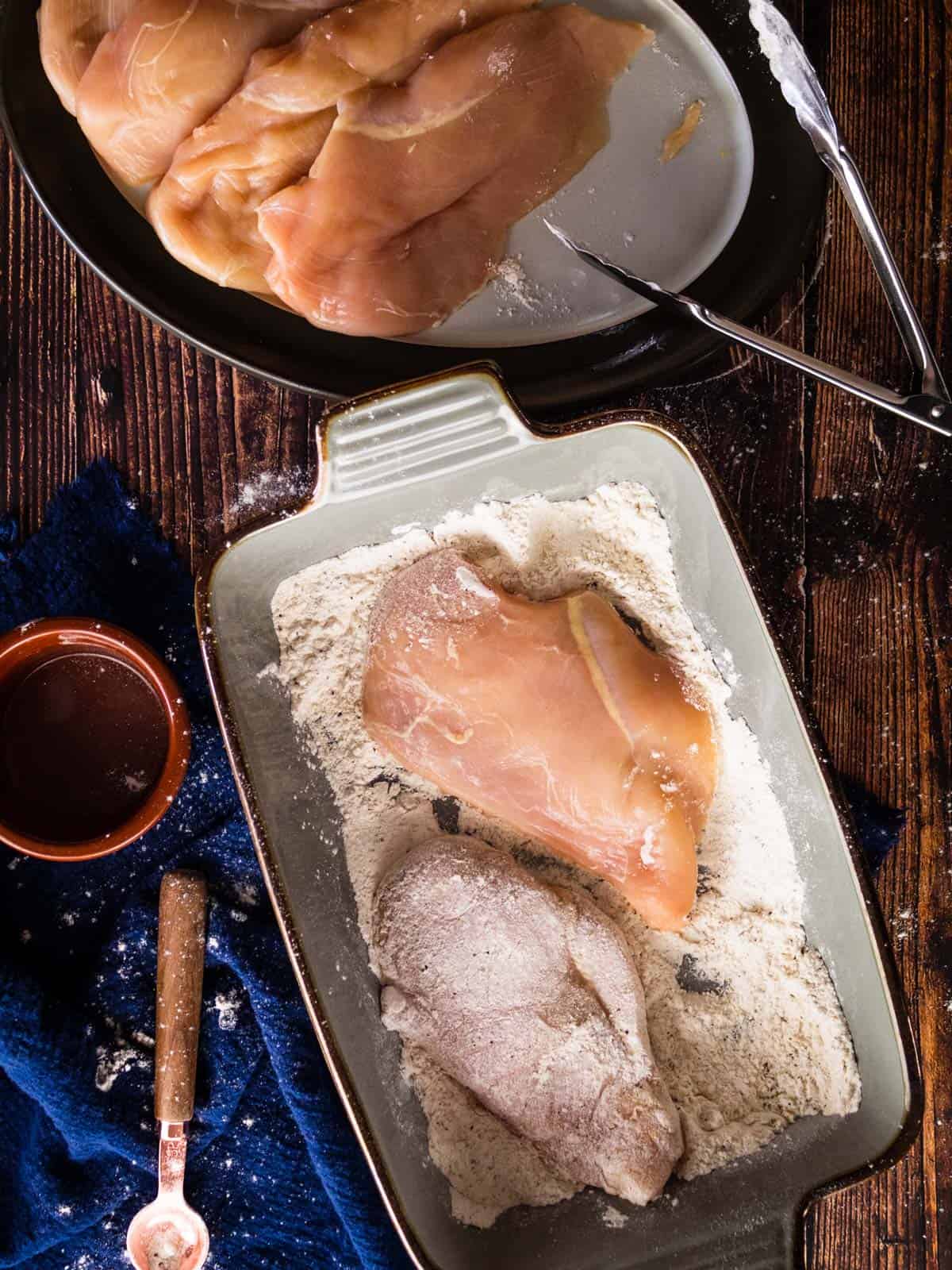 raw chicken on a plate and dipped in flour in a dish.
