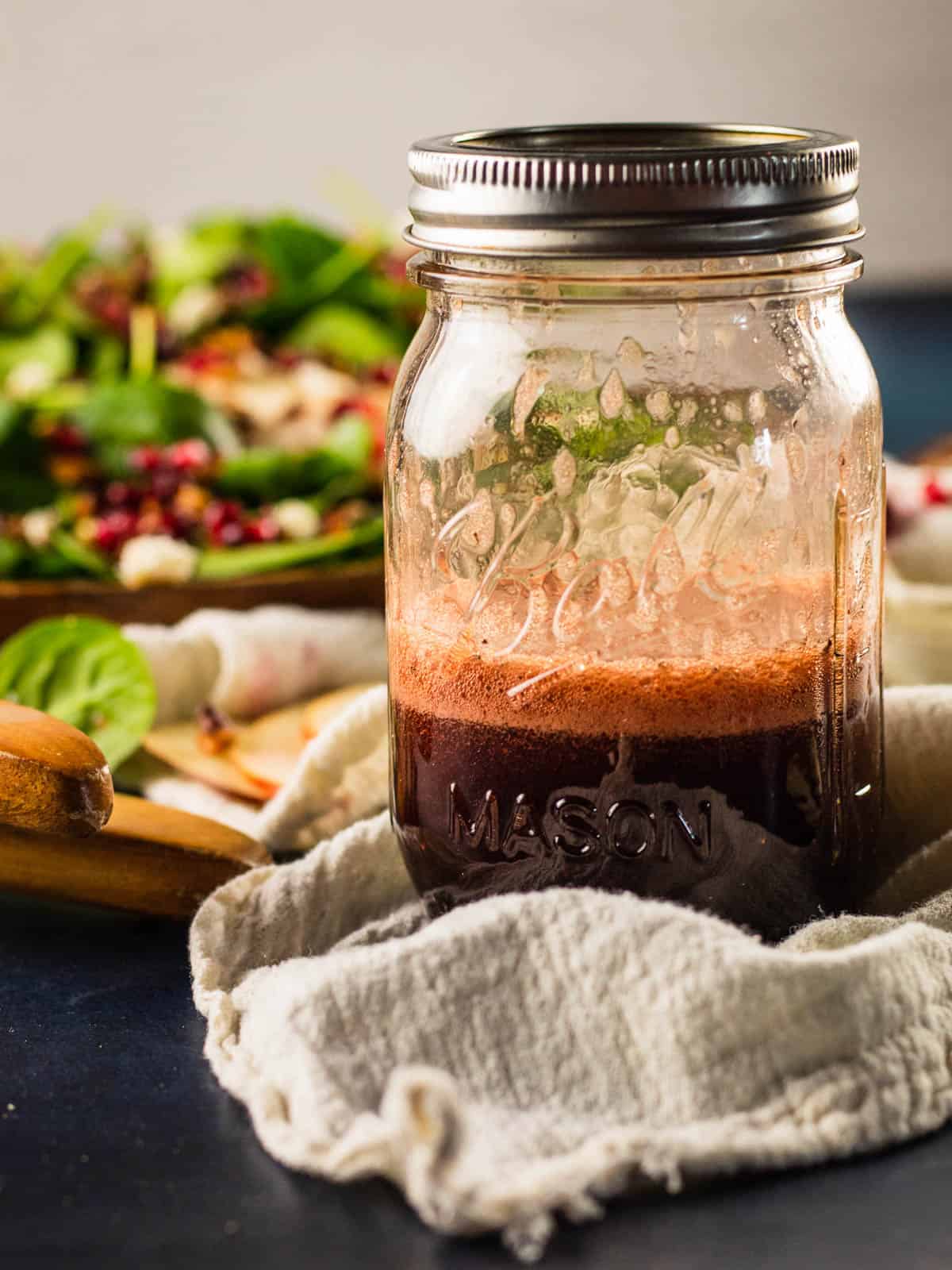 mason jar of homemade salad dressing with a green salad behind it.