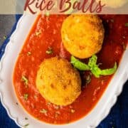 italian rice balls on red sauce with fresh basil on a white oval platter.