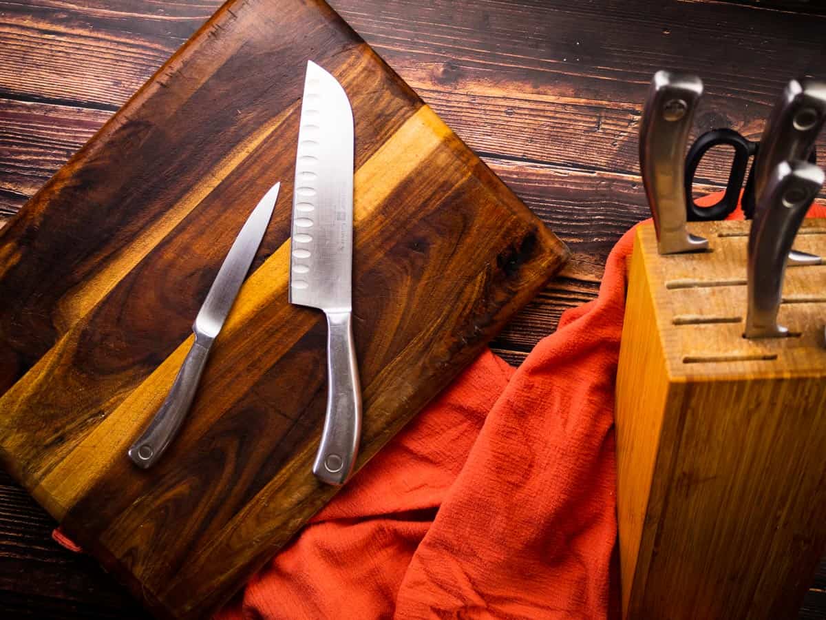 two knives on a cutting board next to knife block with knifes and scissors in them.