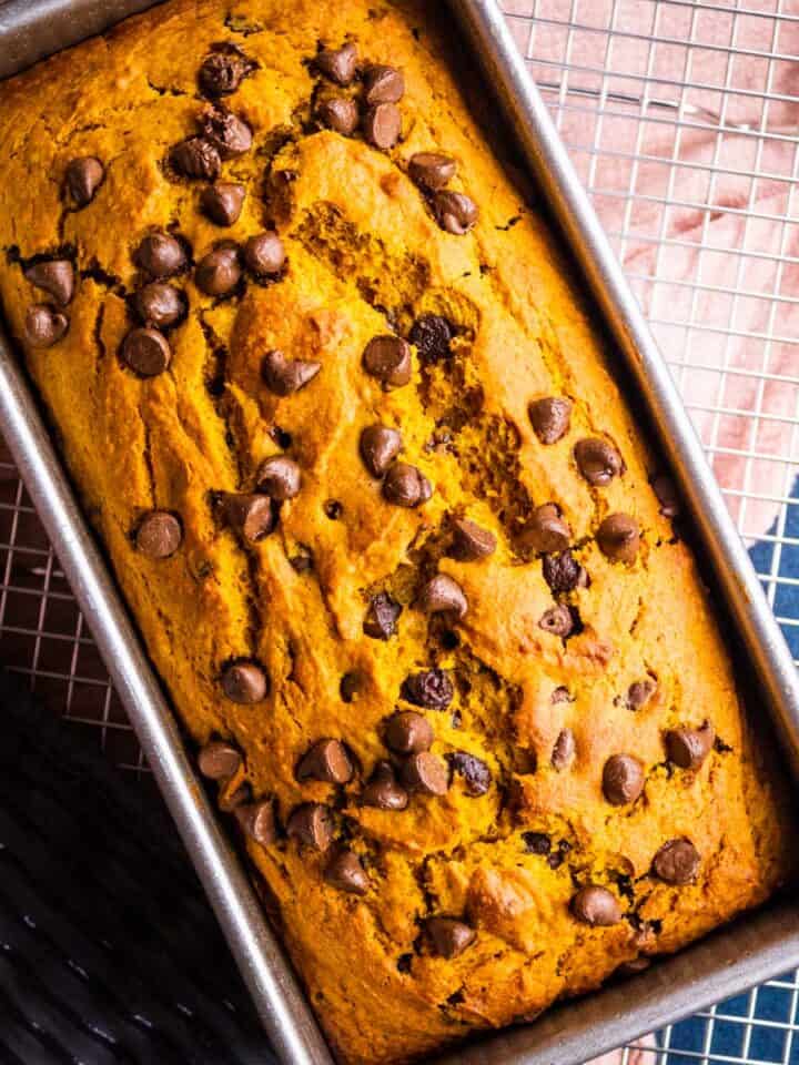 pumpkin chocolate chip bread in a loaf pan on a cooling rack.