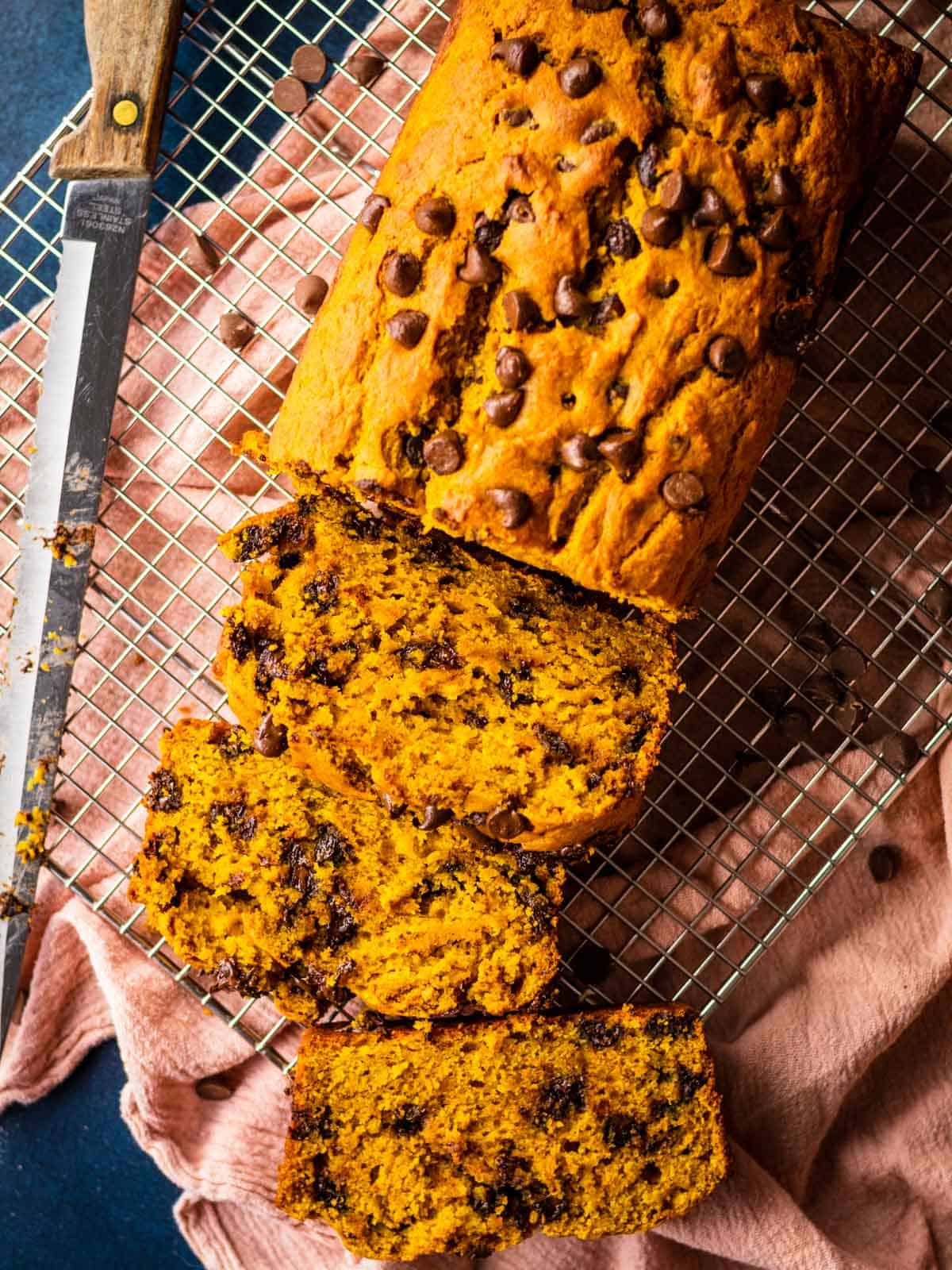 loaf of pumpkin bread with chocolate chips on a cooling rack with a knife, partially sliced.