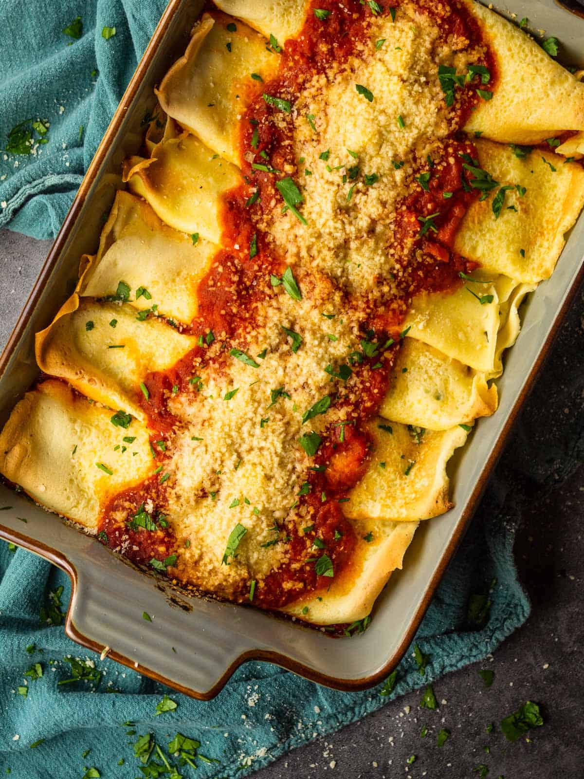 crepe manicotti in a baking dish topped with sauce and cheese down the middle.