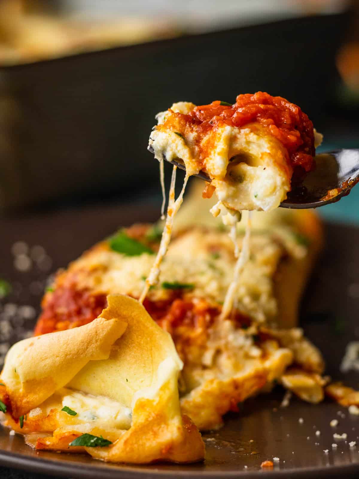 a fork holding a bite of manicotti with cheese pulling from it.