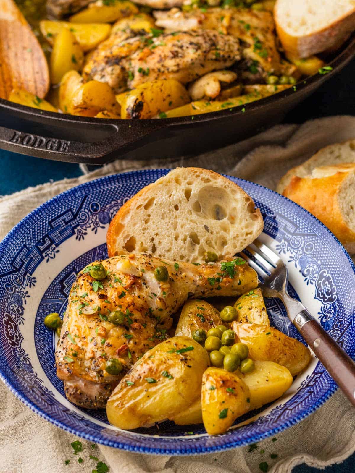 roasted chicken and potatoes with peas in a blue and white bowl with sliced bread.