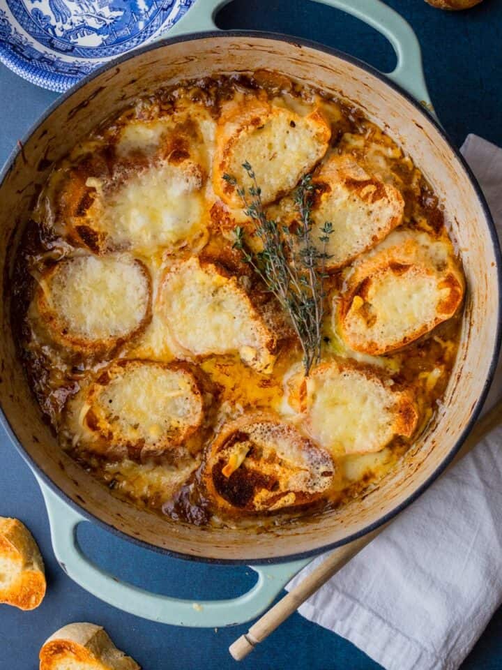 dutch oven pot with french onion soup topped with cheesy bread slices with bowls and spoons.