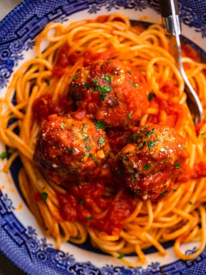 meatballs in red sauce on top of spaghetti sprinkled with parsley and grated cheese.