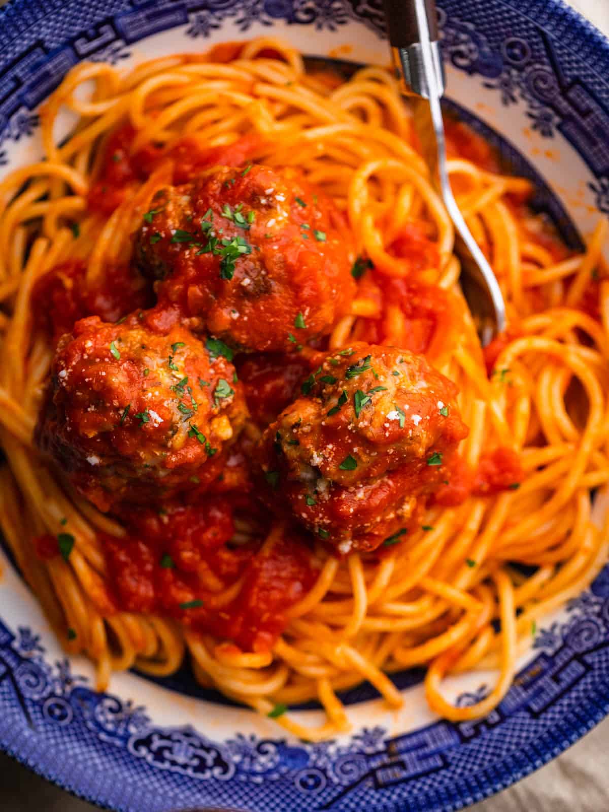 blue bowl with spaghetti and meatballs covered in marinara with parsley and grated cheese.