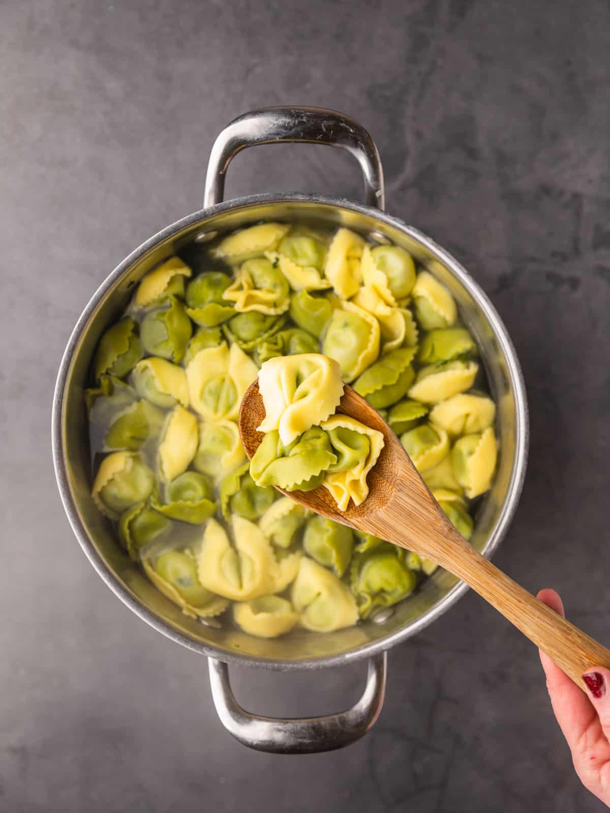 wooden spoon holding a few pieces of cooked spinach and cheese tortellini over a pot.