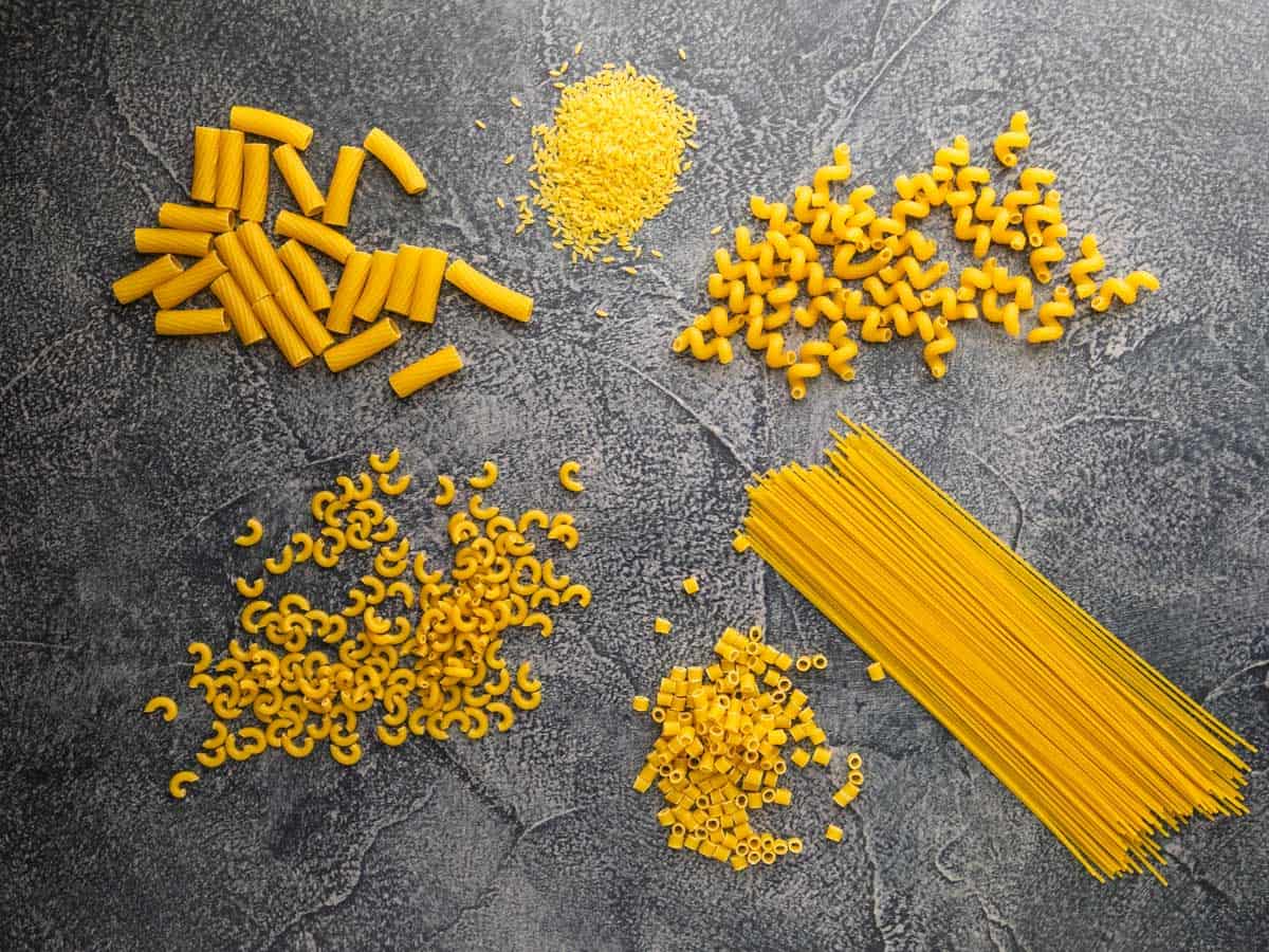 rigatoni, macaroni, ditalini, spaghetti, cavatappi and orzo dried pastas in piles on a table.