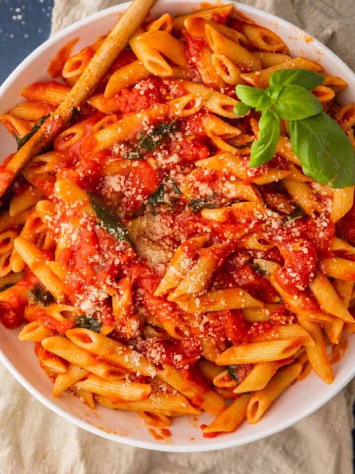 bowl of penne pasta with pomodoro sauce with fresh basil on top.