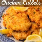 crispy chicken cutlets on a blue and white plate with lemon wedges.