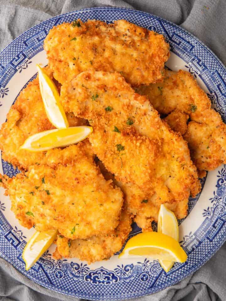 fried chicken cutlets on a blue and white plate with lemon wedges.
