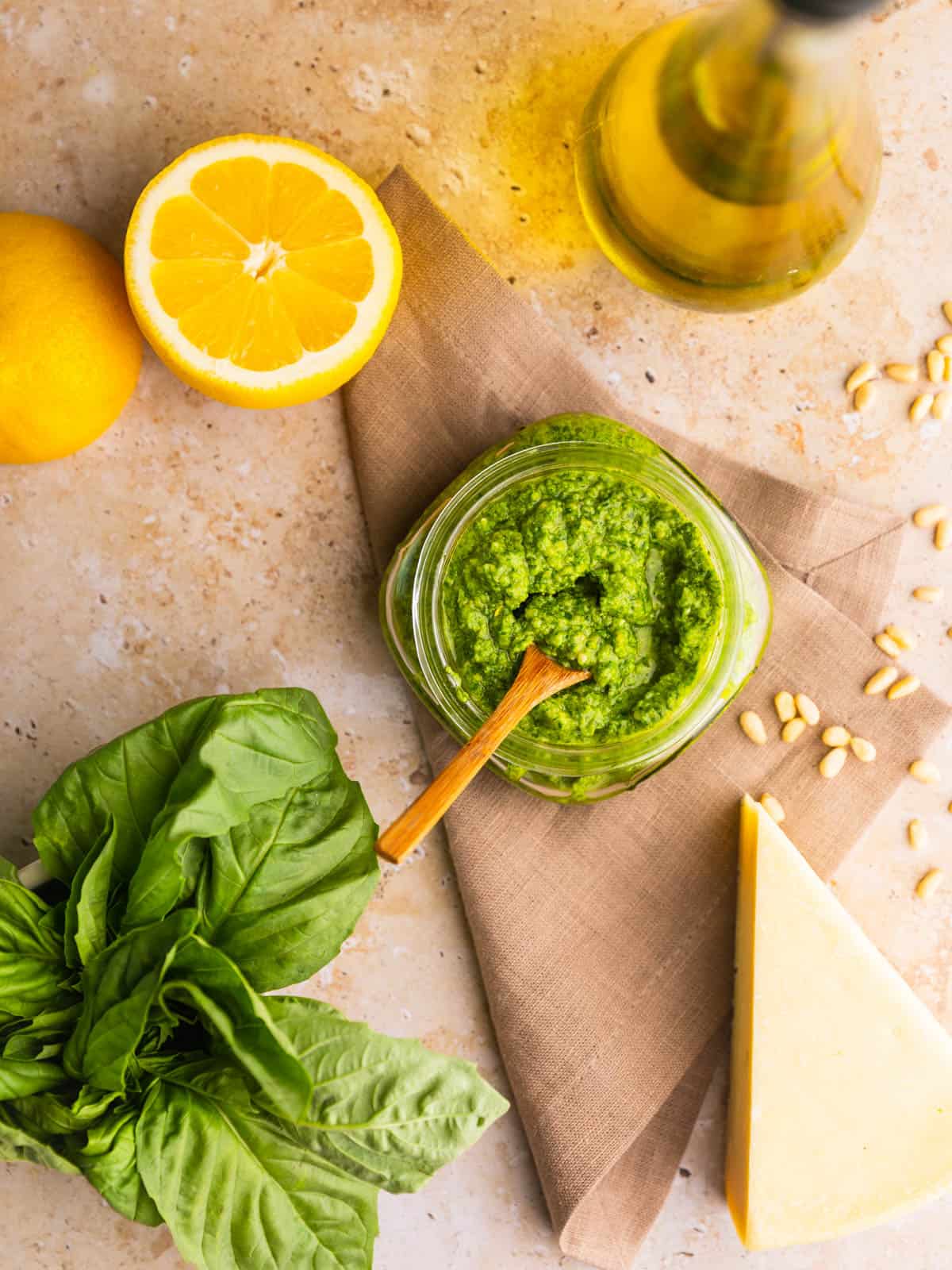 basil pesto in a jar with a wooden spoon with oil, lemons and basil around.