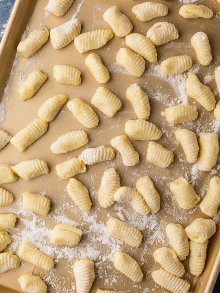 fresh italian gnocchi shaped on a floured gold sheet pan before cooking.