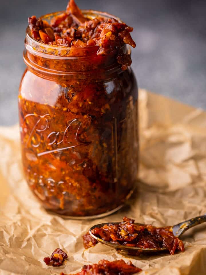 tomato bacon jam in a mason jar with a spoonful next to it on crinkled paper.
