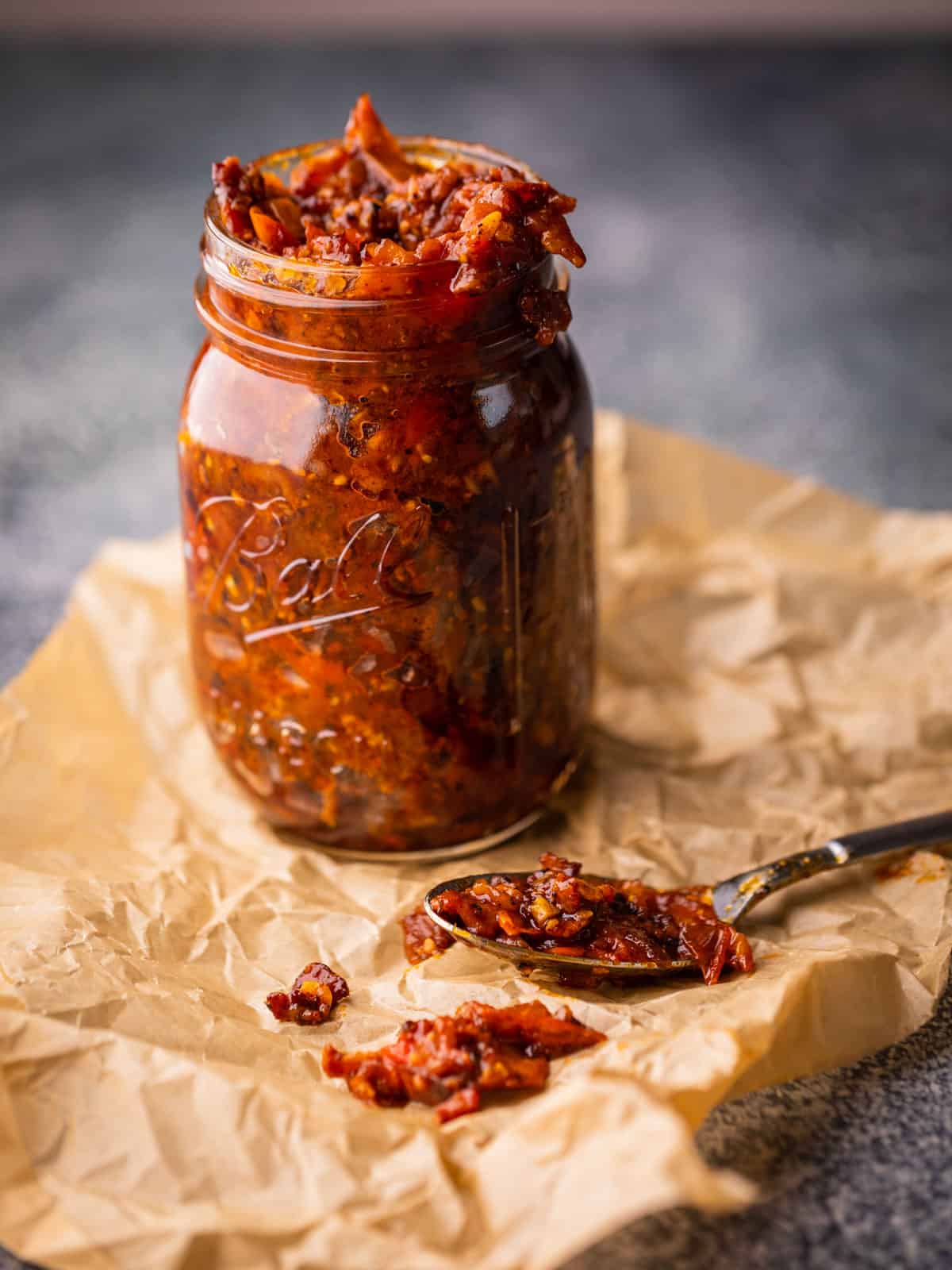 mason jar filled with tomato bacon jam with a spoon of jam lying next to it.
