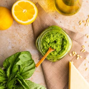 basil pesto in a jar with a wooden spoon with lemon, oil, cheese, nuts and basil.